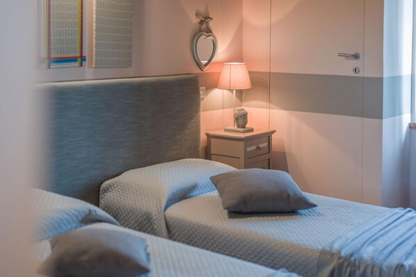 Un dormitorio con dos camas, una mesita de noche con lámpara, un espejo con forma de corazón y una estatua en la pared.