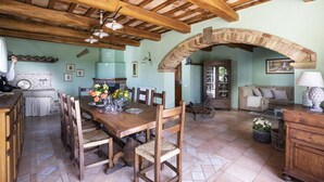 Un coin repas rustique avec une table et des chaises en bois, une cheminée et un espace de vie chaleureux comprenant un canapé et une lampe.