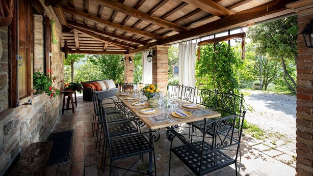 Une terrasse extérieure dotée d’une pergola en bois, de murs en pierre et d’une table dressée pour le repas.