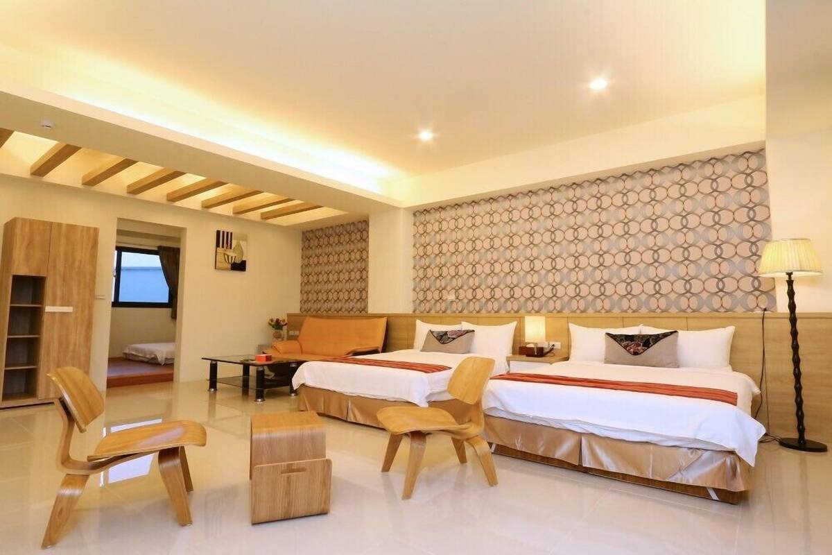 Une chambre d’hôtel moderne avec deux lits, des meubles en bois, une petite table et un mur décoratif.