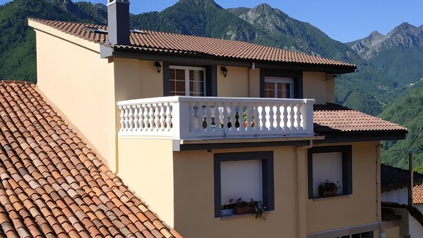 Un bâtiment à deux étages doté d’un balcon, d’un toit en tuiles et surplombant un paysage montagneux.