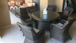 A round glass table surrounded by wicker chairs with cushions, a sofa with orange cushions, and a sliding door in the background. - 3 Bed Apartment Rental w/ Pool nr Beaches, Golf in Vilamoura, Algarve, Portugal (Vilamoura)