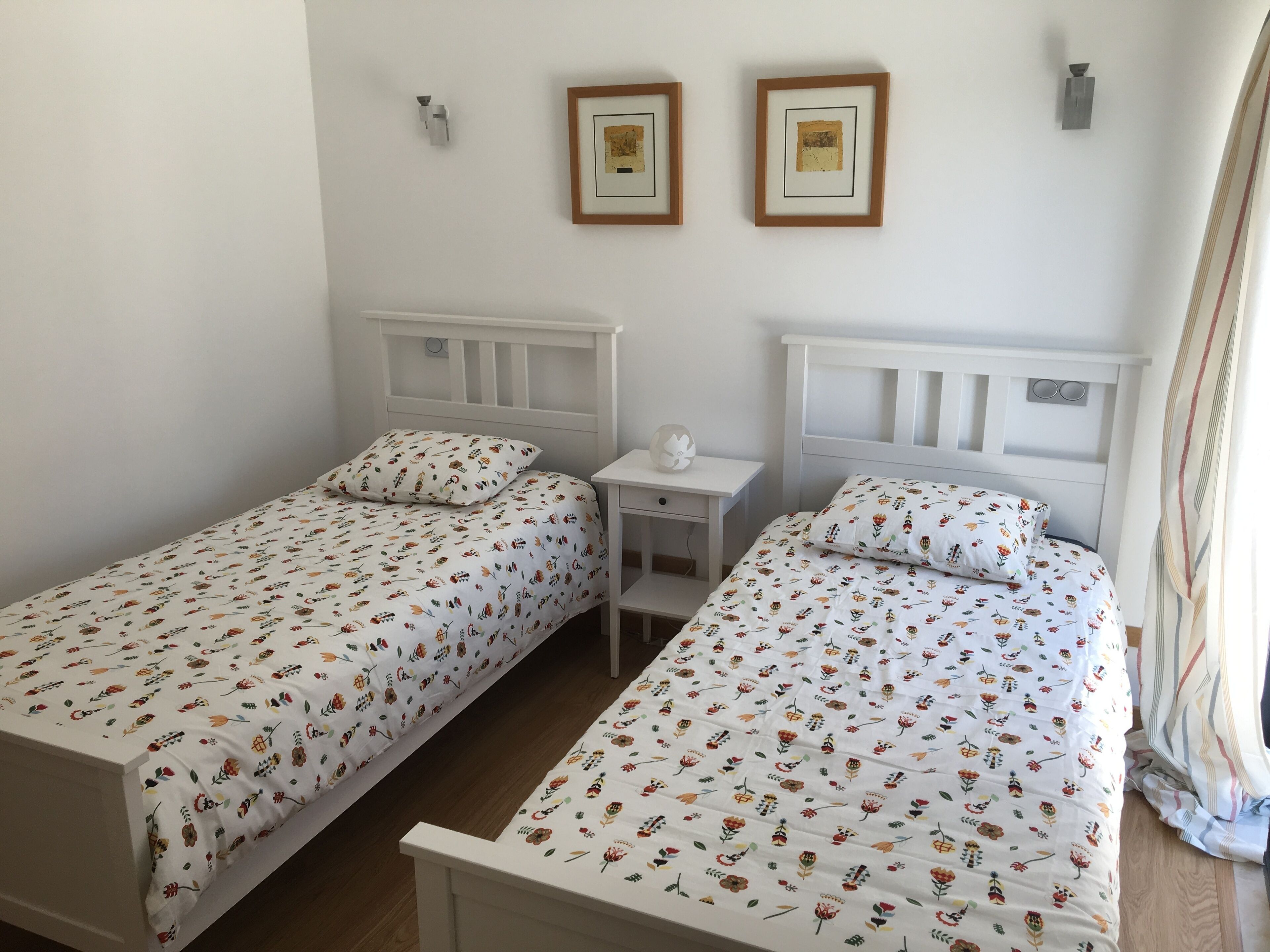 Two single beds with floral bedding, white headboards, and bedside tables with lamps.
