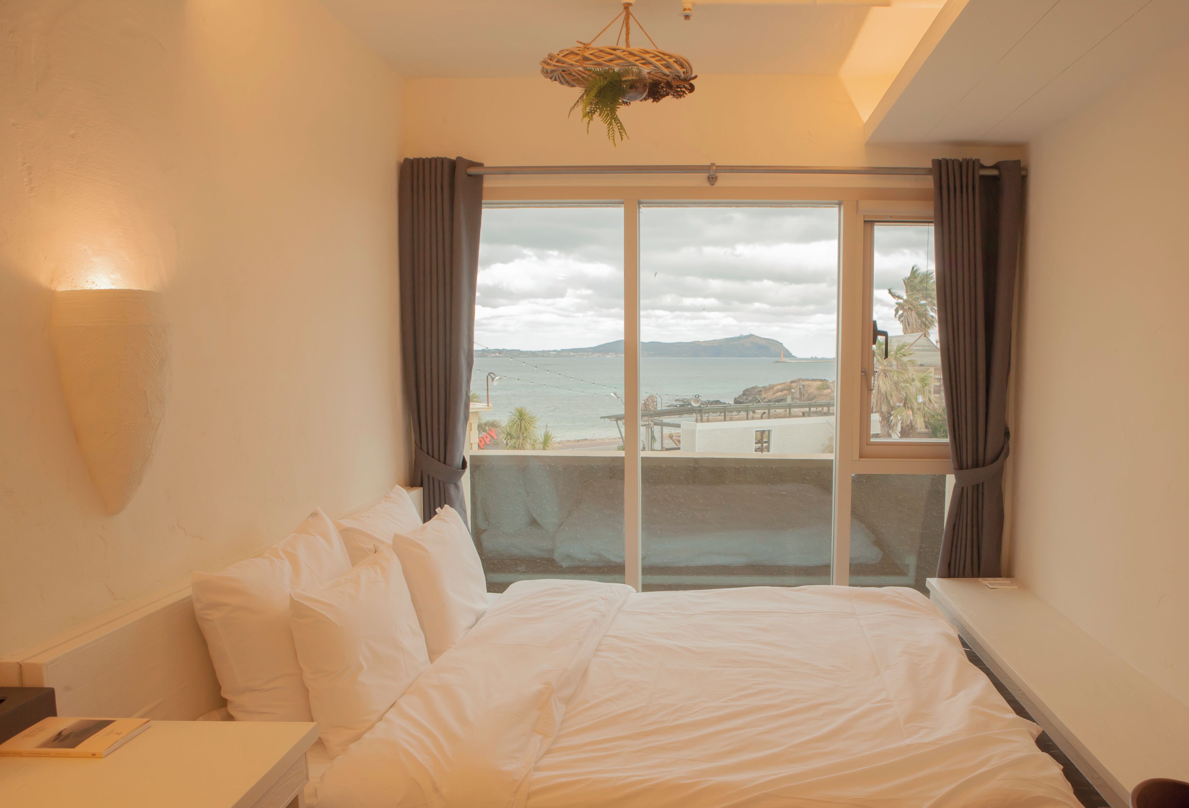 A hotel room with a large bed, a view of the sea, and a hanging light fixture.
