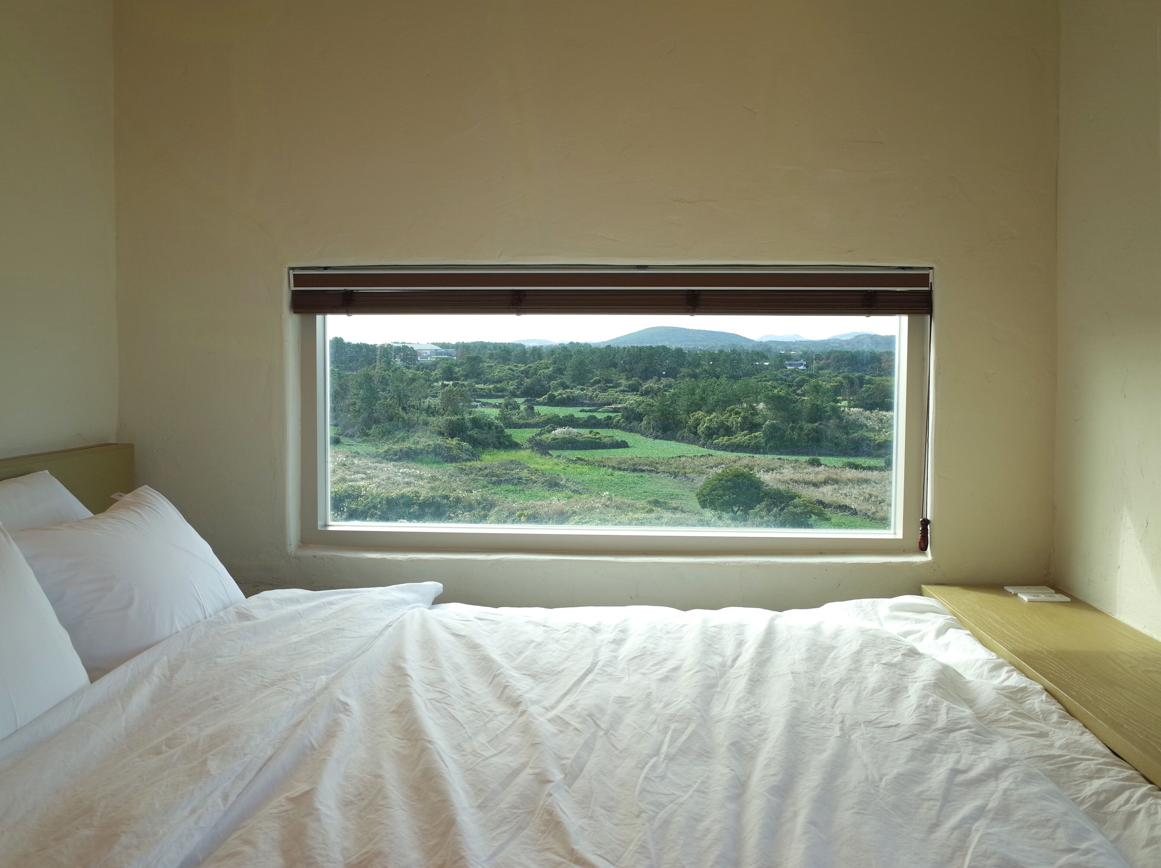 Un dormitorio con un amplio ventanal que ofrece vistas a un paisaje verde y colinas.