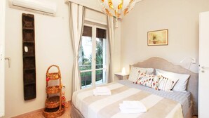 Un dormitorio con cama, mesita de noche, lámpara colgante, ventana con cortinas y aire acondicionado instalado en la pared.