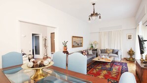 Un salón amplio con una mesa de comedor de cristal, un conjunto de sofás, una alfombra estampada y una araña.