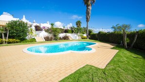 A swimming pool with a curved edge, surrounded by a brick patio and a well-maintained lawn. - Carrell White Villa, Pool, Wifi (Lagos)