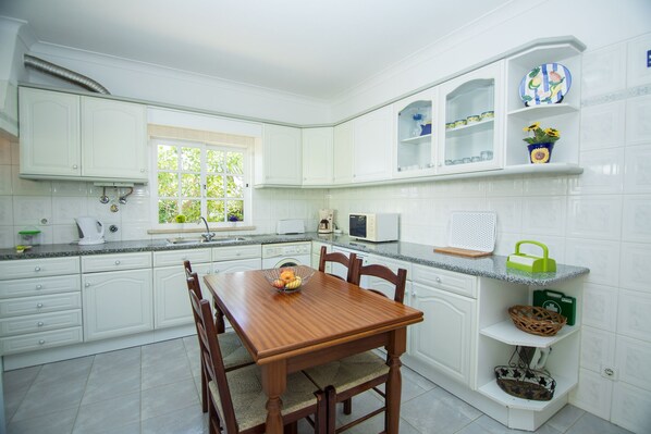A kitchen with white cabinets, a wooden dining table, and a window. - Carrell White Villa, Pool, Wifi (Lagos)