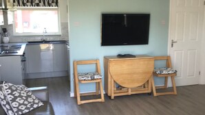A living room with a sofa, two wooden chairs, a TV, and a kitchen in the background. - LEE'S CHALET, NORTON PARK, Dartmouth, 2 bedrooms, sleeps 4 (Dartmouth)