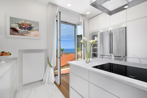 A modern kitchen with a large window, white cabinetry, and a stainless steel refrigerator.