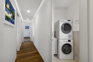 A laundry room with two stacked washing machines and a hallway leading to another room.