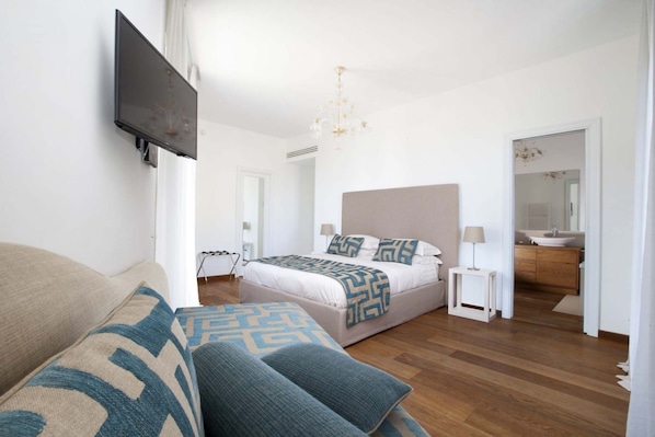A modern bedroom with a large bed, bedside tables, a TV mounted on the wall, and a bathroom visible through an open door.