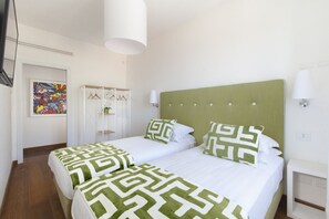 Une chambre d’hôtel avec deux lits, chacun recouvert d’une couvre-lit à motifs verts et blancs, doté d’une tête de lit verte et de lampes blanches fixées au mur.