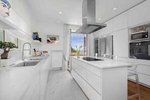 Una cocina moderna con armarios blancos, una isla grande, electrodomésticos de acero inoxidable y vistas al exterior.
