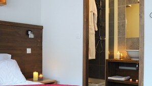 Ein Hotelzimmer mit Bett, Nachttisch, Holz-Kopfteil, Badezimmer mit Dusche, Waschbecken und Spiegel.