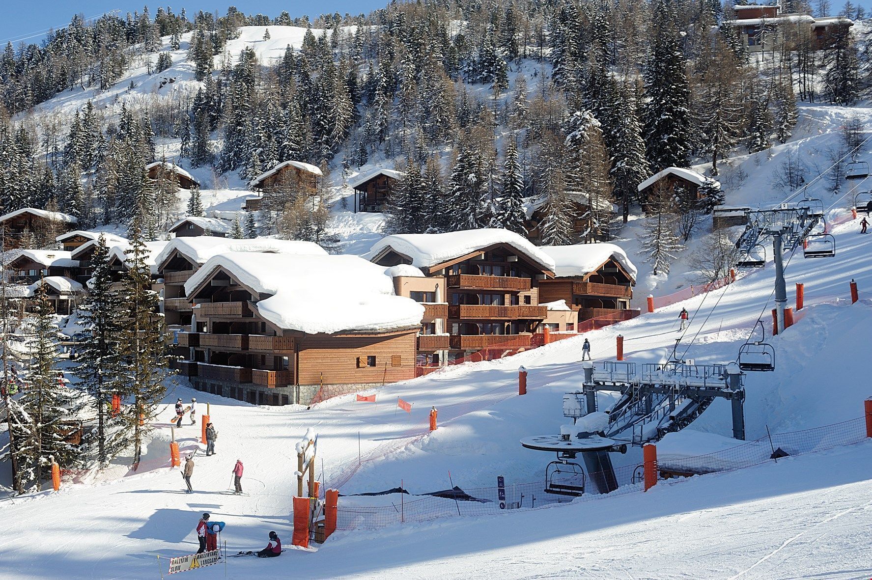 A ski resort with wooden lodges, a ski lift, and a snowy landscape.