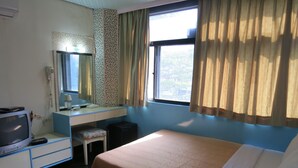 A hotel room with a bed, a desk with a television, a mirror, and a window with curtains. - Reui Cheng Hotel (Kaohsiung)