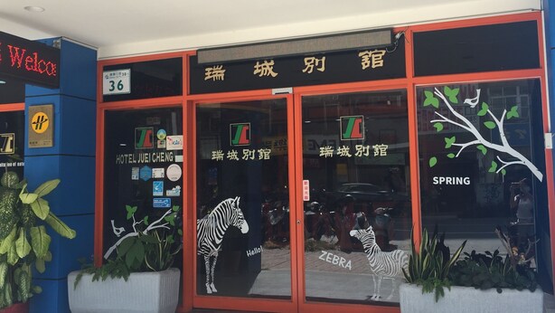A hotel entrance with signage in a foreign language, a zebra decal on the glass, and potted plants outside. - Reui Cheng Hotel (Kaohsiung)