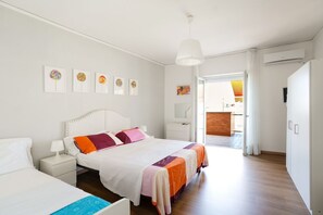 A hotel room with a bed, bedside tables, a hanging light fixture, artwork on the wall, and a view of the outside.