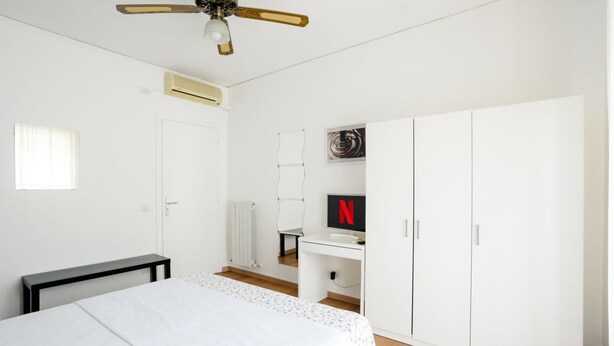 Una camera da letto con un letto, una scrivania, un armadio, una ventola a soffitto e un condizionatore d'aria.