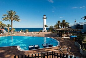 Un espace piscine avec des chaises longues, un phare et une vue sur l’océan.