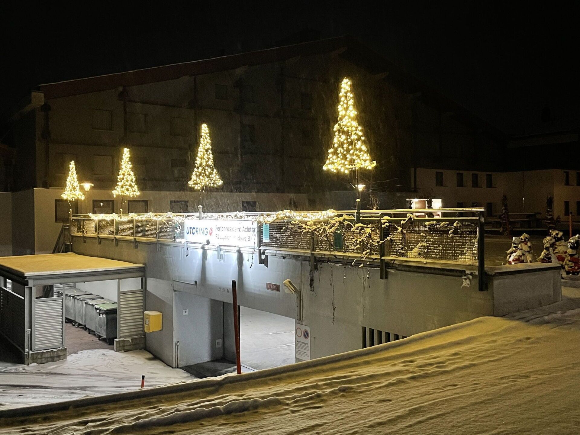 A building with three illuminated Christmas trees, a covered outdoor area, and a sign with text.
