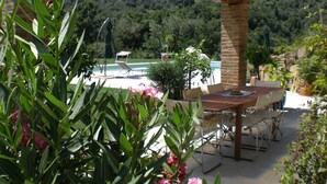 Un patio al aire libre con piscina, rodeado de exuberante vegetación y una pérgola de madera.