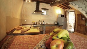 Una cocina con estufa, lavamanos y armarios de madera. Hay un frutero en la encimera con plátanos, manzanas y un melón.
