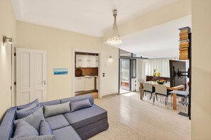 A modern living room with a sofa, a dining area with a table and chairs, a kitchen with cabinets, and a staircase leading to an upper floor.