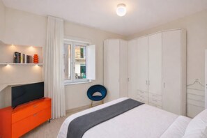 Una camera da letto con un letto, una televisione su una cassettiera, un armadio e una finestra con tende.