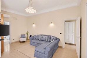 A living room with a sectional sofa, a television, a small white chair, and a chandelier.