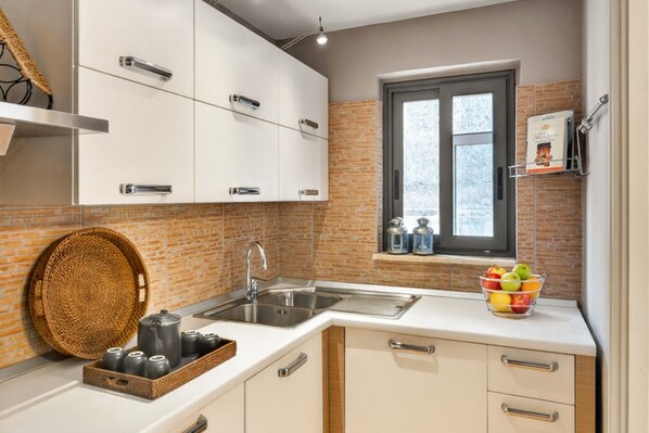 A kitchen with white cabinets, a brick backsplash, a window, and a fruit bowl on the counter.