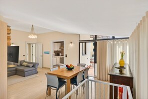 A modern living room with a sofa, dining table, and a kitchen area visible through an open door.