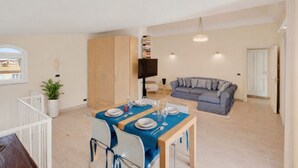 Un comedor con una mesa para dos personas, un sofá, un televisor y una estantería en un apartamento moderno.