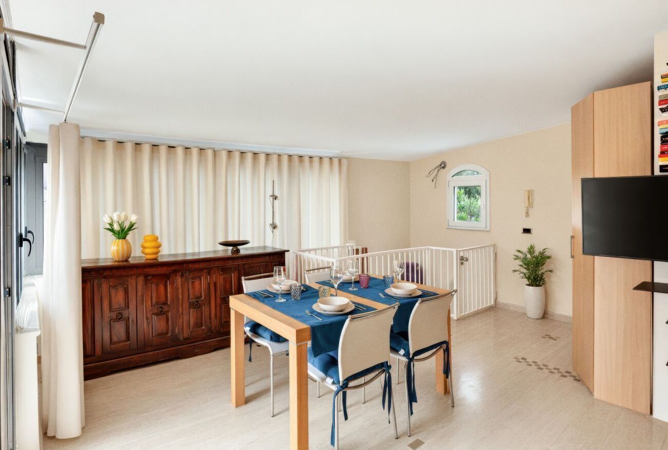Un comedor con una mesa dispuesta para cuatro personas, un armario de madera, un radiador y un televisor a la derecha.