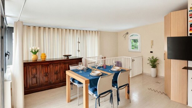 Un comedor con una mesa dispuesta para cuatro personas, un armario de madera, un radiador y un televisor a la derecha.