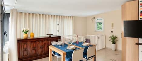 Un comedor con una mesa dispuesta para cuatro personas, un armario de madera, un radiador y un televisor a la derecha.