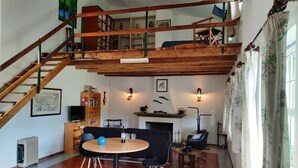 Ein geräumiges Zimmer mit einer Holztreppe, einem Essbereich mit rundem Tisch und einem Kamin.