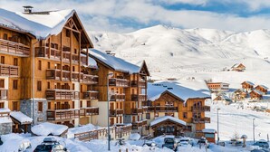Un complejo turístico en la montaña cubierto de nieve, con edificios de madera, pistas de esquí y cielo despejado.