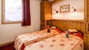 Una habitación acogedora con dos camas, una ventana que ofrece vistas a las montañas, paredes de madera y un pequeño estante con adornos.