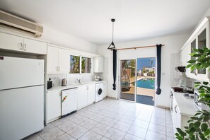 A modern kitchen with white cabinets, a built-in washing machine, and a view of a swimming pool. - Villa Jazmin, Lovely 4BDR Protaras Villa with Pool,2 minute walk to Fig Tree Bay (Protaras)