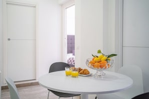 Una mesa de comedor con un frutero, dos vasos de zumo de naranja y cruasanes.