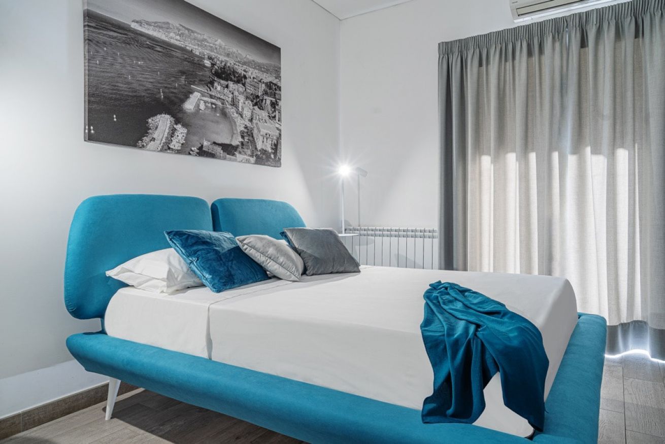 A modern bedroom with a bed, a blue sofa, and a large window with curtains.