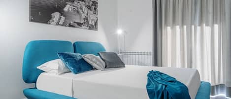 Ein modernes Schlafzimmer mit einem Bett, einem blauen Sofa und einem großen Fenster mit Vorhängen.
