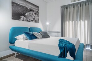 A modern bedroom with a bed, a blue sofa, and a large window with curtains.