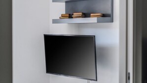 Ein modernes Interieur mit einem an der Wand befestigten Flachbildfernseher, über einem grauen Regal mit Büchern und Dekorationsobjekten.