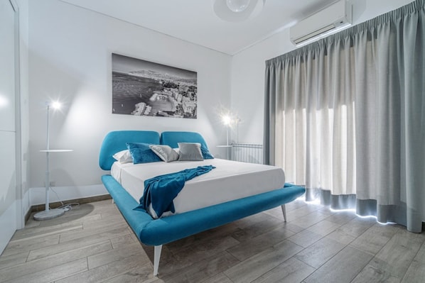 Un dormitorio moderno con una cama, una lámpara de pie y un gran ventanal con cortinas.