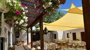 An outdoor dining area with tables and chairs, surrounded by potted plants and a pergola with hanging flowers. - ALQUERIA DE GÍTAR. Beautiful rural villa for 20 people close to the sea (Felix)