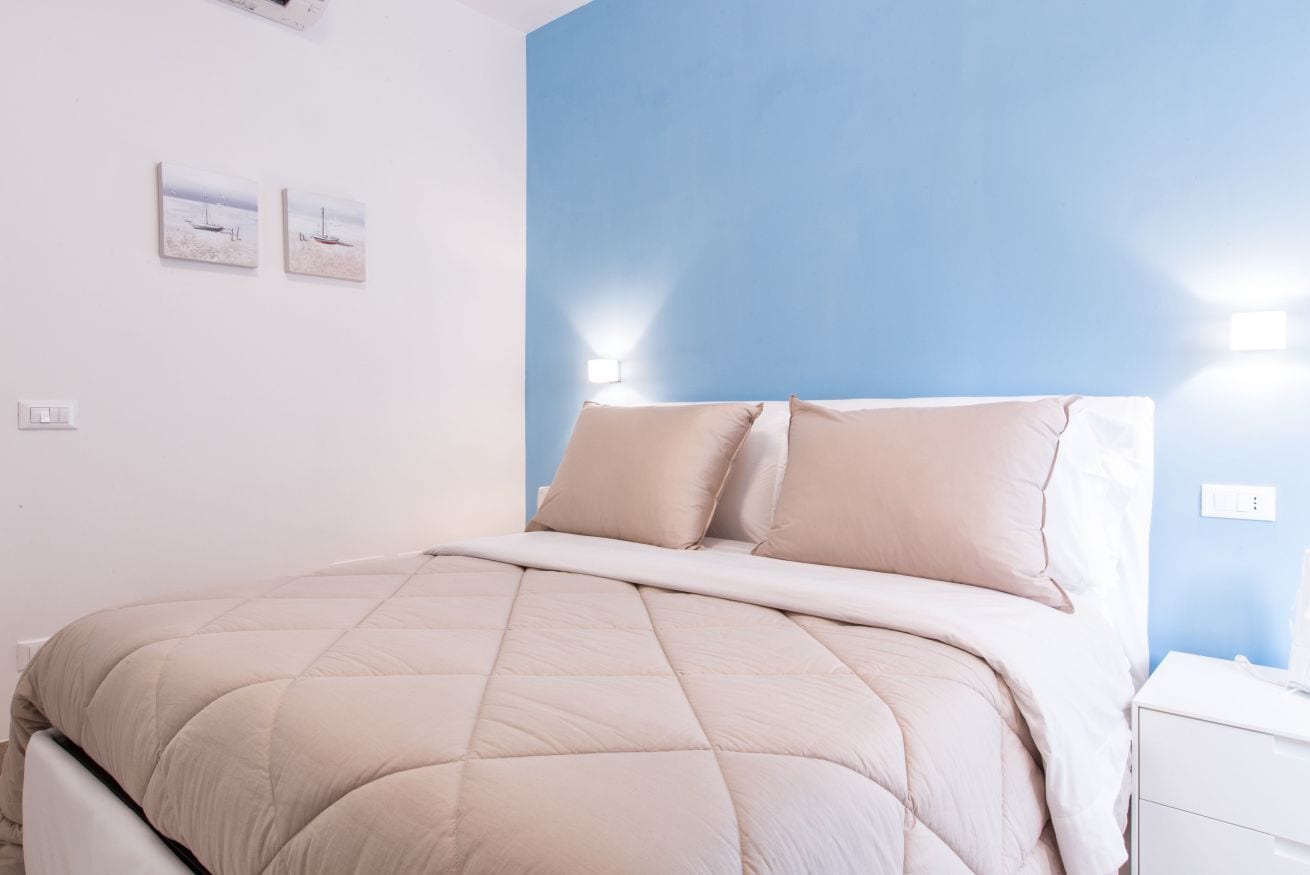 A bedroom with a bed, a nightstand, and a wall-mounted light.